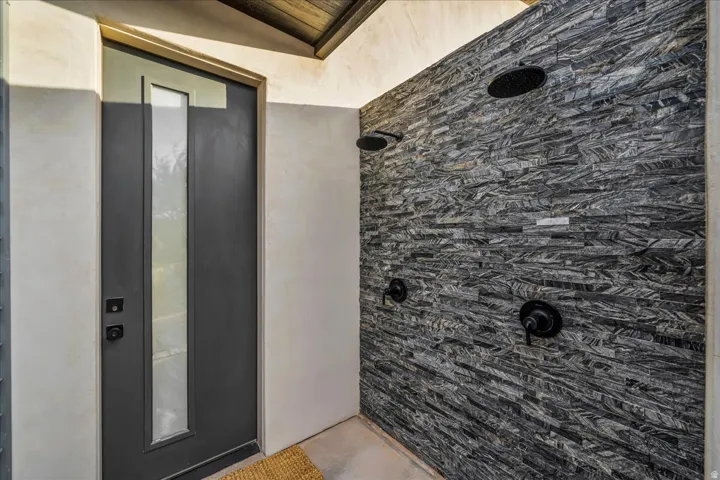Outdoor shower featuring a textured stone-finish wall, dual matte black rain shower heads, and coordinating matte black controls