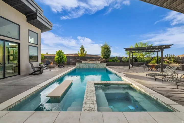 Outdoor swimming pool with integrated spa and sun shelf, a pergola, and a fire pit area