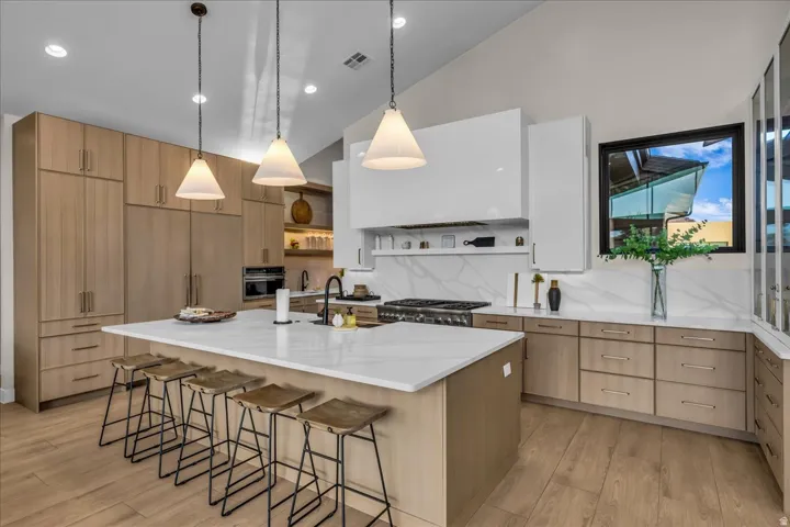 Spacious kitchen featuring a large central island with seating, integrated appliances, wood-finish cabinetry, and a vaulted ceiling with pendant lighting