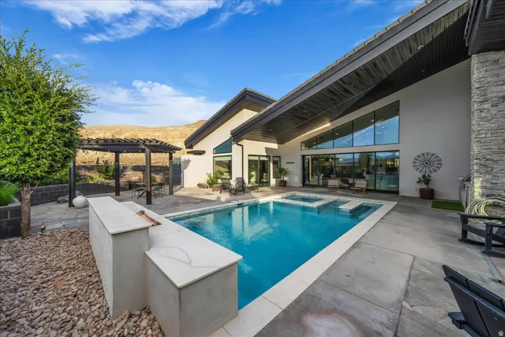 Outdoor living area featuring a rectangular pool with an integrated spa, a pergola-covered patio, and a built-in fire feature