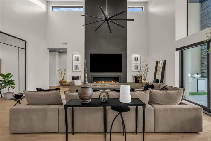 Soaring ceilings with transom windows, a floor-to-ceiling fireplace with integrated media, wood-finish flooring, and expansive glass sliding doors