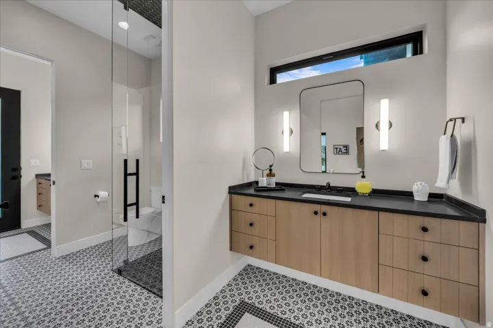 Floating wood-finish vanity with black countertop, rectangular mirror, and sconce lighting