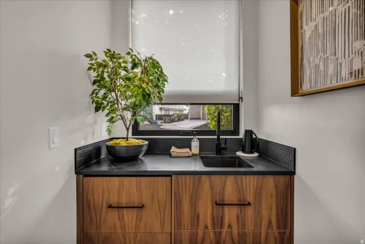 Custom wood-finish cabinetry with dark hardware, black countertop, integrated black sink with matching faucet, and textured black tile backsplash
