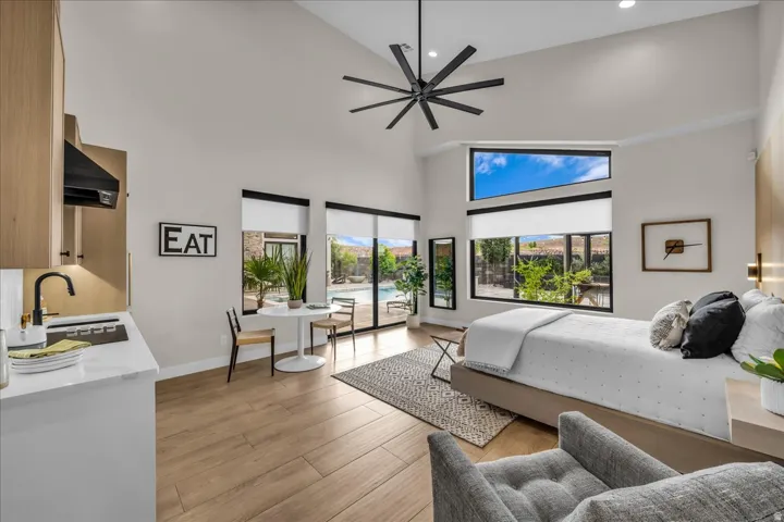 Vaulted ceiling with an oversized ceiling fan, wood-finish flooring, full-height windows, a built-in cooktop, and a wall-mounted range hood