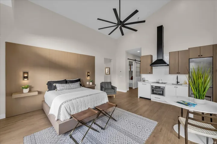 Vaulted ceiling with a large ceiling fan, integrated kitchen with stainless steel appliances, wood-finish flooring, and built-in wall sconces