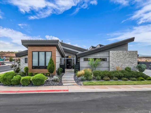 Modern architectural design featuring varied rooflines, a stone walkway, multi-pane windows, wood-finish paneling, and an integrated stone wall
