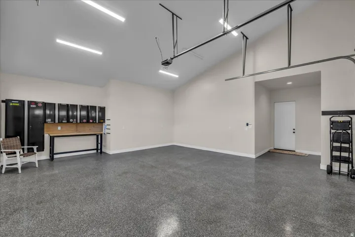 Vaulted ceiling garage with epoxy flooring, task lighting, and built-in wall storage