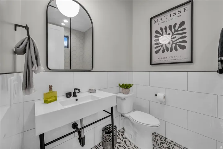 Wall-mounted vanity sink with matte black faucet, framed arched mirror, white subway tile wainscoting, and patterned hexagonal floor tiles