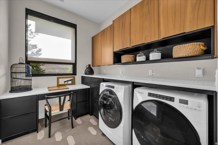 Modern laundry area featuring wood-finish cabinetry, black base cabinets, white countertops, and a full-height tile backsplash