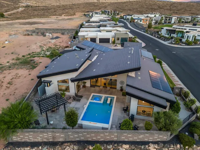 Modern exterior architecture with an angular roofline, integrated solar panels, and a backyard featuring a swimming pool with an elevated spa, an outdoor patio, and a shaded pergola