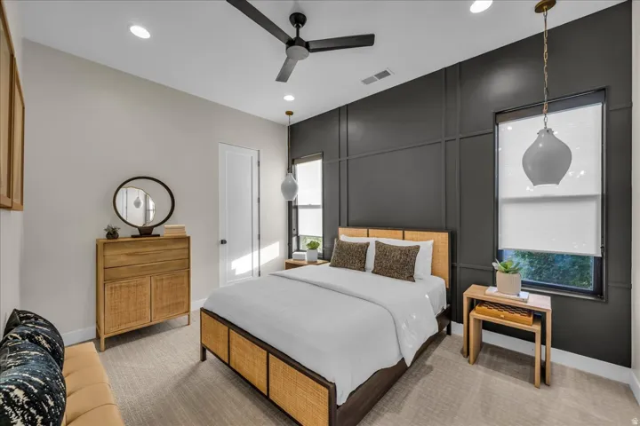 Recessed lighting, ceiling fan, accent wall with panel molding, two windows with roller shades, and carpet flooring