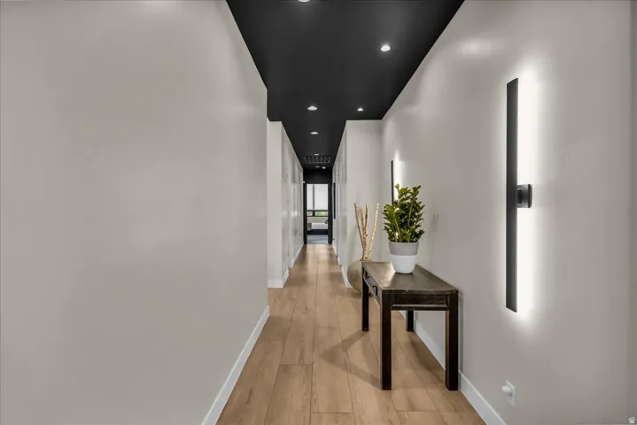 Hallway featuring light wood-finish flooring, recessed ceiling lighting, and linear wall sconces