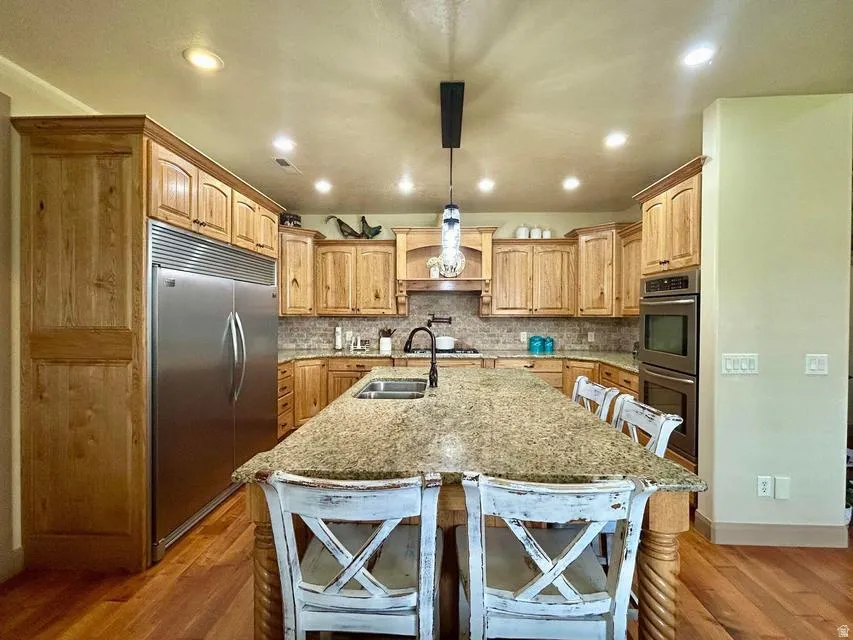 Spacious kitchen featuring natural wood cabinetry, stainless steel double ovens, a built-in refrigerator, a large island with a stone-finish countertop, and recessed lighting