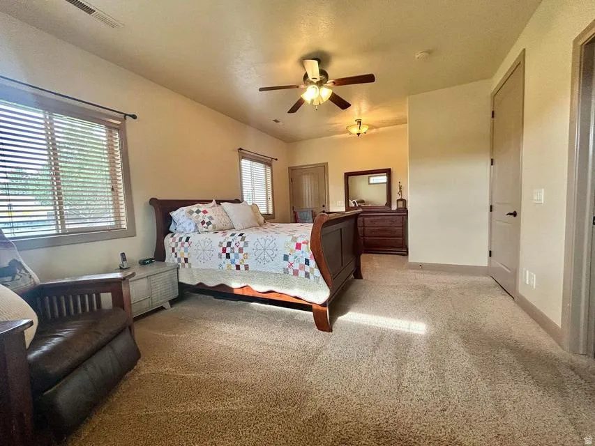 Carpeted room featuring multiple windows with blinds, a ceiling fan, and painted interior doors