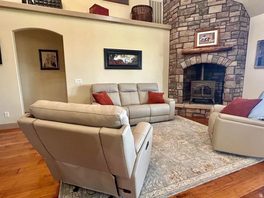 Stone-clad fireplace with a wood-burning stove, solid wood flooring, and an arched doorway