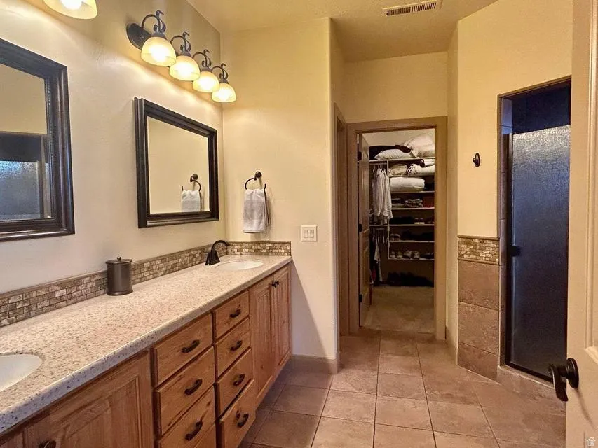 Dual vanity with integrated sinks, mosaic tile backsplash, wood-finish cabinetry, tile flooring, and a walk-in shower with a glass enclosure