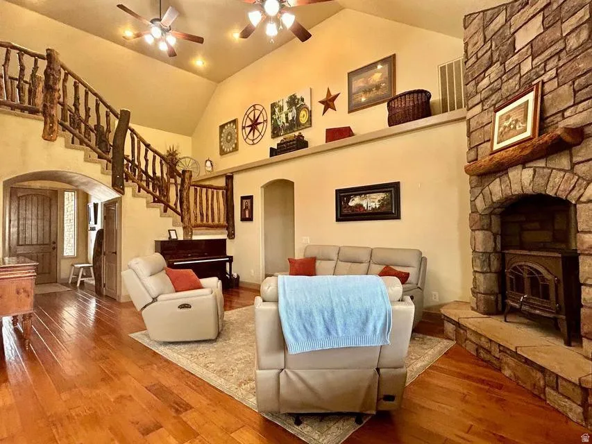 Vaulted ceiling with multiple ceiling fans, natural wood-finish flooring, stone-clad fireplace with hearth and wood mantel, custom wood-log staircase, and arched entryways