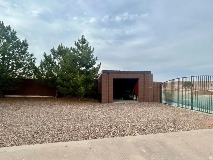 Gravel landscaping with evergreen trees, a block storage structure, and a fenced-in swimming pool