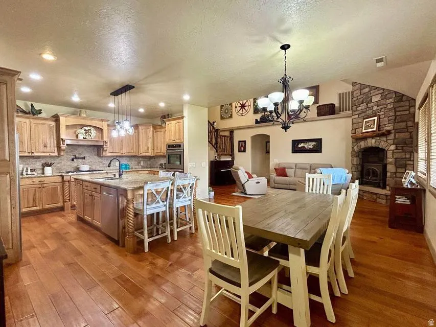 Open-concept living space with wood-finish flooring, a stone fireplace, and an expansive kitchen island with bar seating