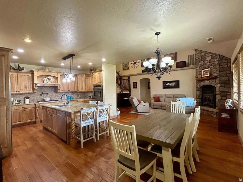 Hardwood flooring throughout, a kitchen island with seating, a stone-front fireplace, recessed lighting, and a vaulted ceiling