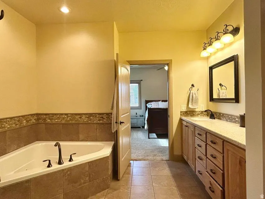 Corner soaking tub with tile surround, dual sink vanity with wood cabinetry, and a framed mirror with overhead lighting