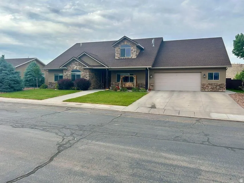 Stucco exterior with stone accents, attached two-car garage, mature landscaping, and a pitched shingle roof