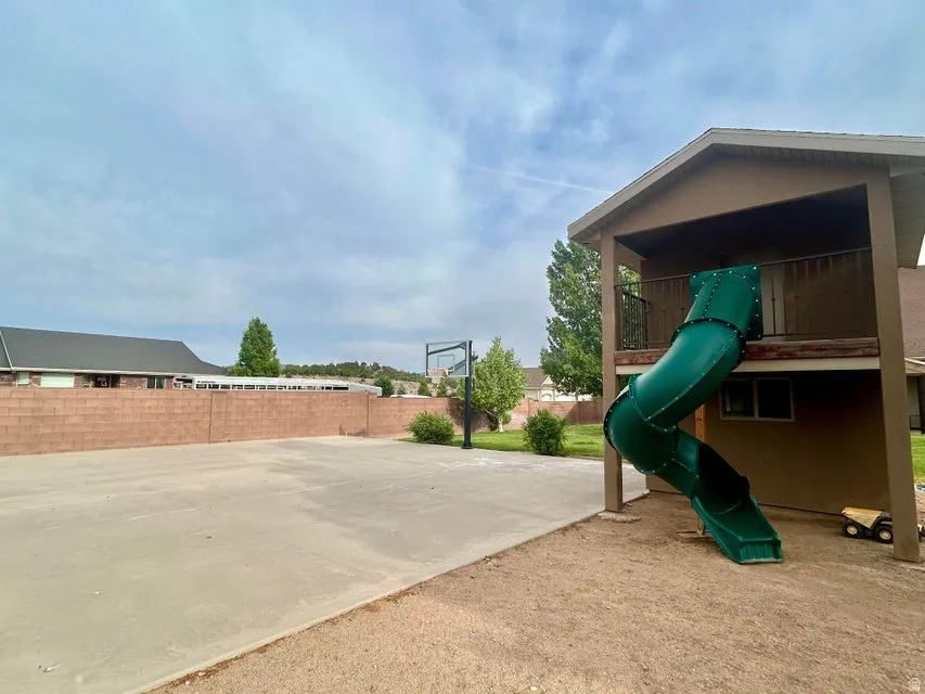 Expansive concrete court with an integrated basketball hoop, brick privacy wall, and a multi-level structure featuring an enclosed slide