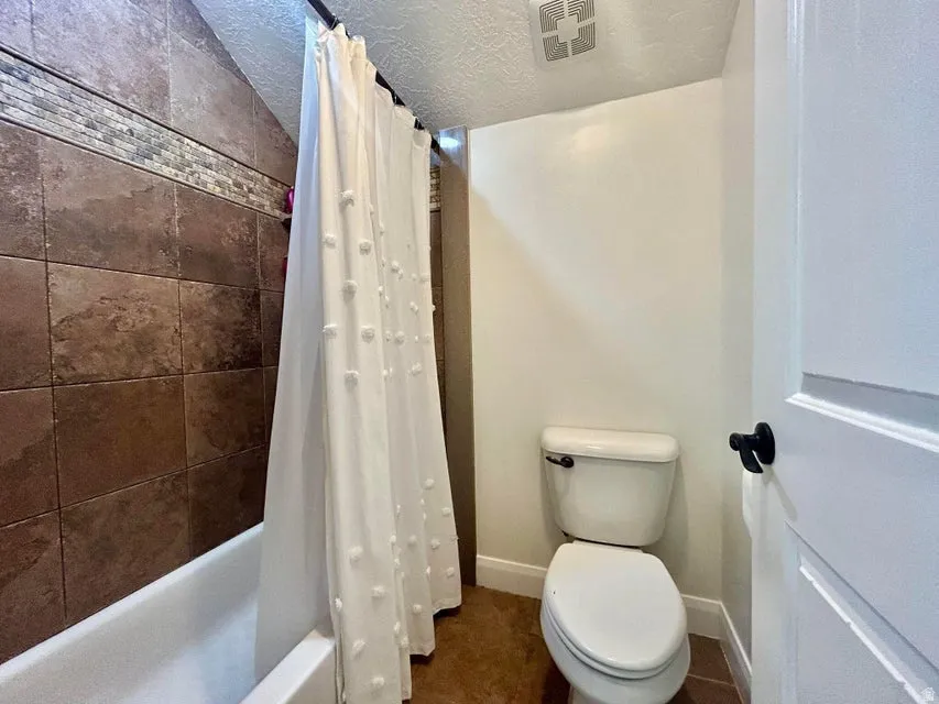 Tub-shower combination with full-height tile surround, decorative mosaic tile accent, and a white toilet