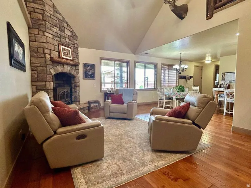 Vaulted ceiling, stone-clad fireplace with wood stove insert, rich wood flooring, and recessed lighting