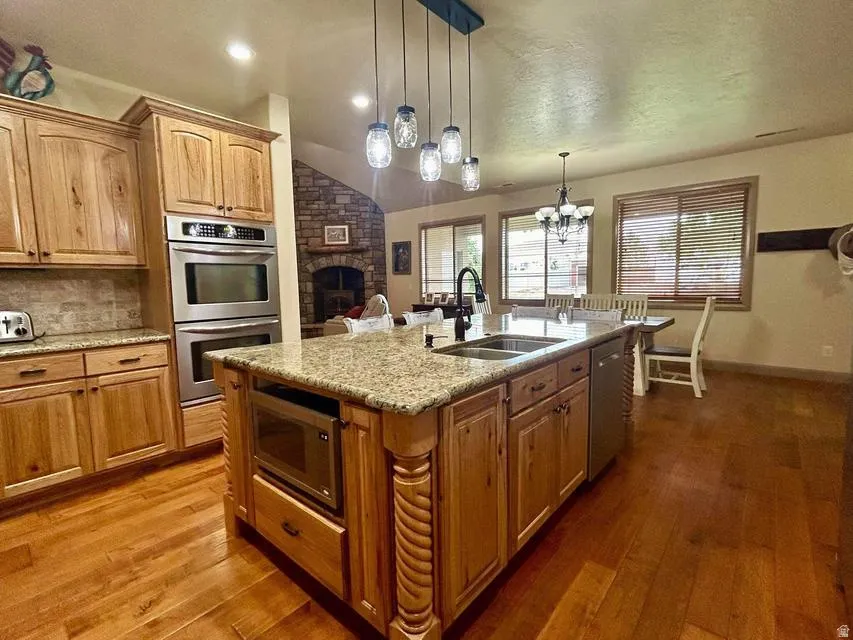 Wood-finish flooring, granite countertops, stainless steel double wall ovens, built-in microwave, and a stone-clad fireplace