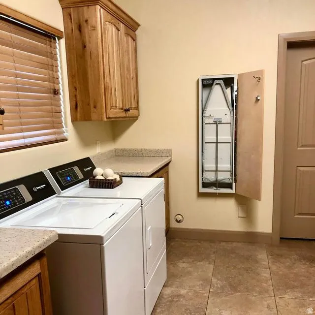 Functional laundry space featuring durable tile flooring, wood-finish cabinetry, and solid surface countertops