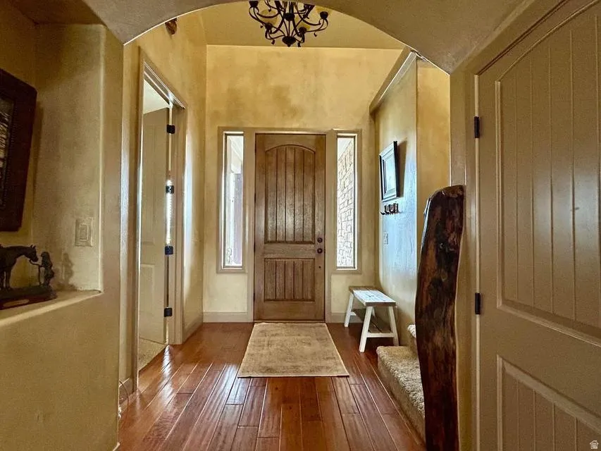 Arched entryway featuring wood-finish flooring, a paneled wooden door, and wrought iron chandelier