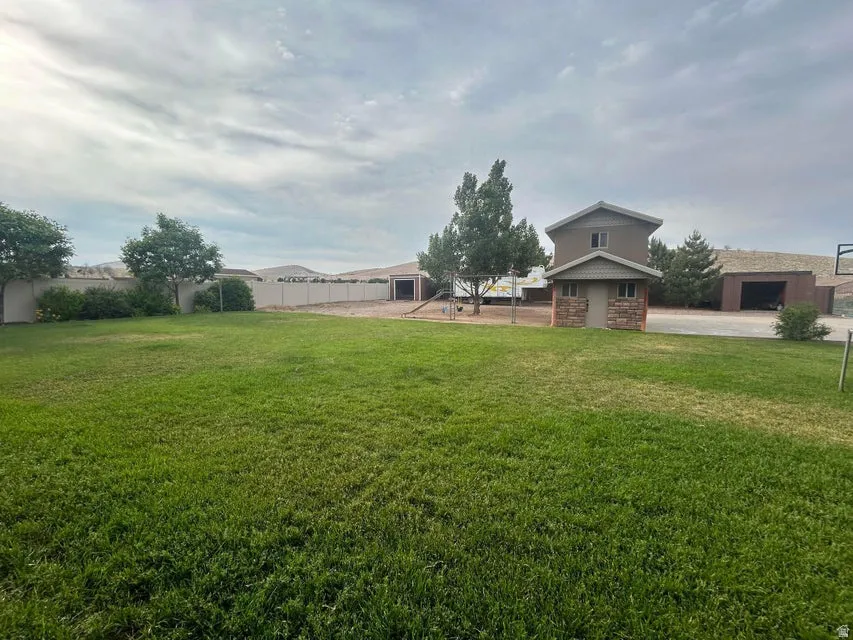 Expansive grassy yard with a concrete block privacy fence, mature trees, and a detached structure featuring stone veneer and siding