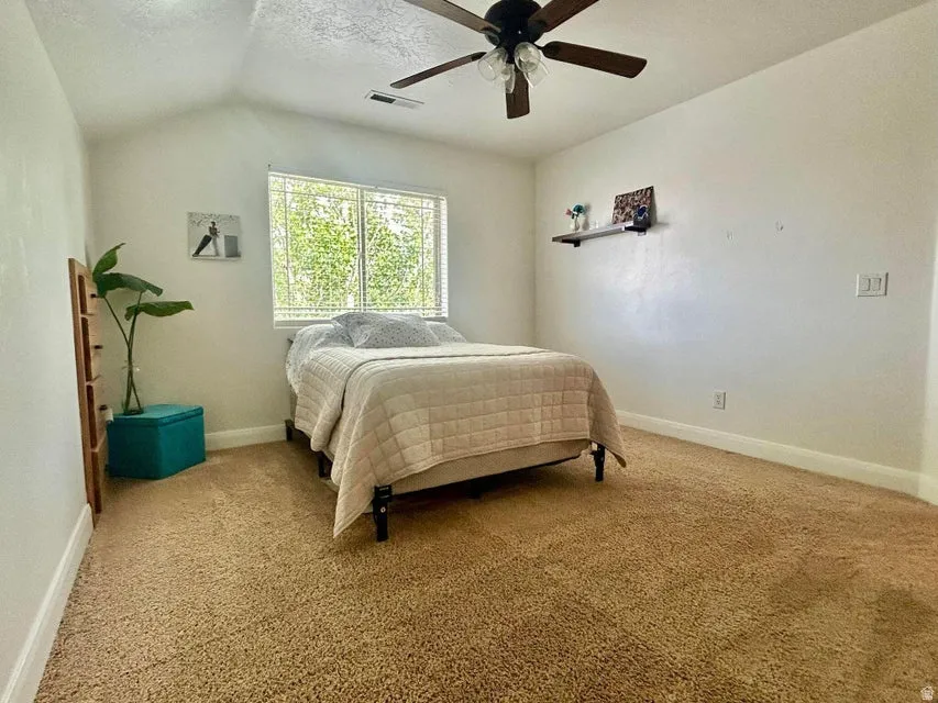 Vaulted ceiling with a ceiling fan, carpeted flooring, and a large window