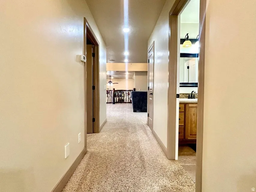 Carpeted hallway with recessed lighting, neutral wall tones, and wood-finish door frames