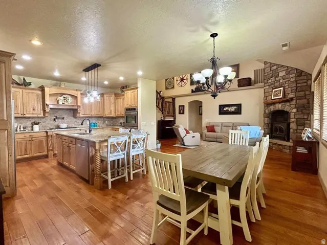 Open-concept living space with wood-finish flooring, a stone fireplace, and an expansive kitchen island with bar seating