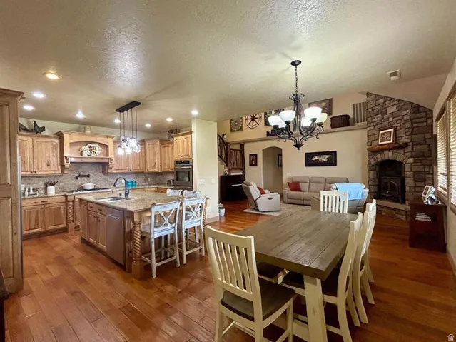 Hardwood flooring throughout, a kitchen island with seating, a stone-front fireplace, recessed lighting, and a vaulted ceiling