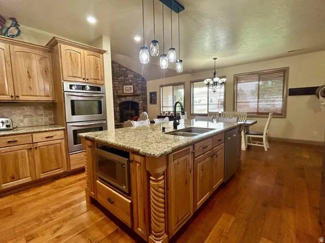 Wood-finish flooring, granite countertops, stainless steel double wall ovens, built-in microwave, and a stone-clad fireplace