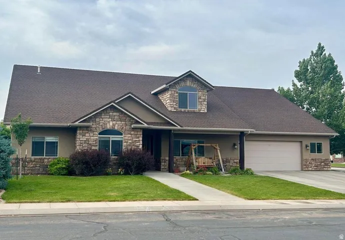 Stucco exterior featuring stone accents, a dormer window, and an attached two-car garage