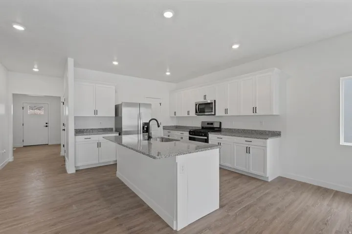 Kitchen featuring white cabinetry, granite countertops, stainless steel appliances, a center island with a sink, and wood-finish flooring