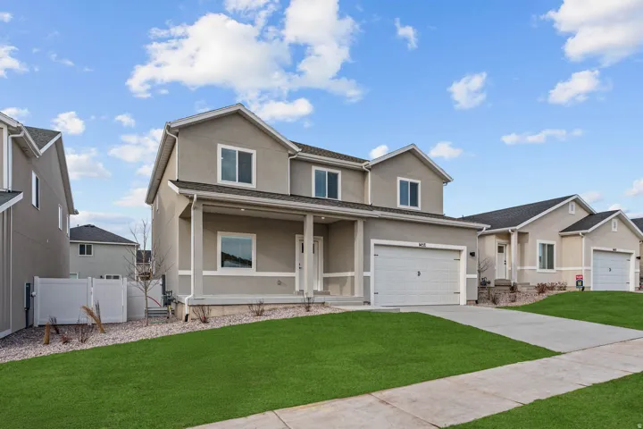 Stucco exterior with a covered porch, attached garage, concrete driveway, and a front lawn with landscaping