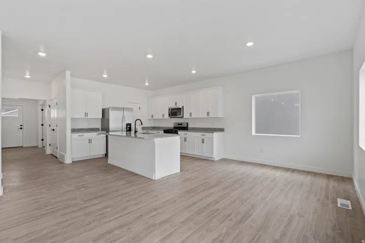 Open-concept kitchen and living area featuring white cabinetry, a central island with a sink, stainless steel appliances, and wood-finish flooring