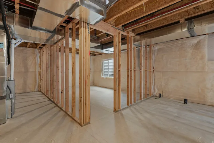 Unfinished basement featuring wood framing, exposed ductwork, concrete flooring, and a window with horizontal blinds