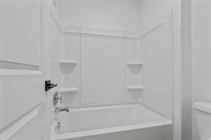 White bathtub with integrated wall surround and storage shelves, accented by a chrome faucet and matte black door hardware
