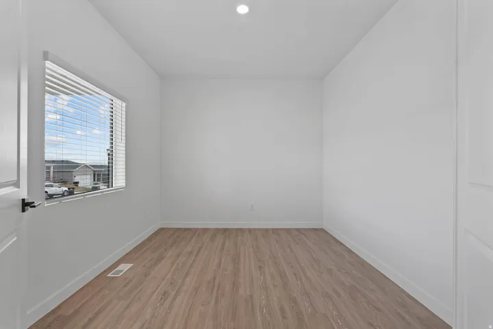 Bright interior with wood-finish flooring, white walls, and a single window with horizontal blinds