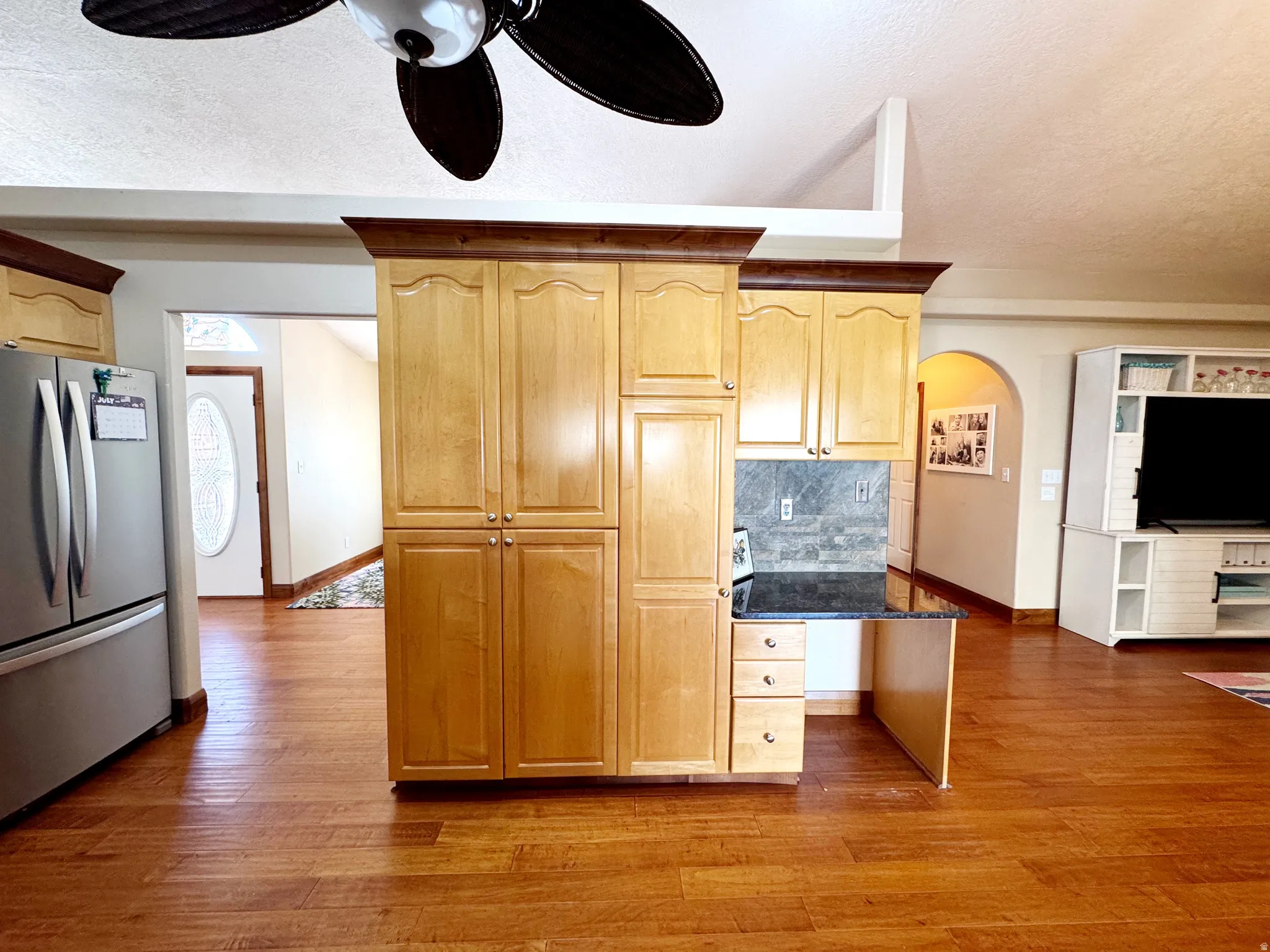 Wood-finish flooring throughout, vaulted ceiling, built-in cabinetry, stainless steel refrigerator, and ceiling fan