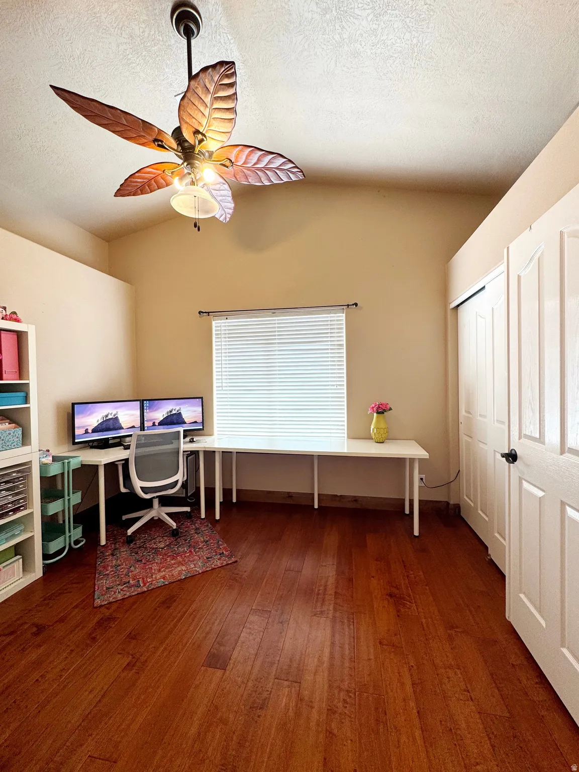 Vaulted ceiling with an attached ceiling fan, rich wood-finish flooring, and a window with blinds