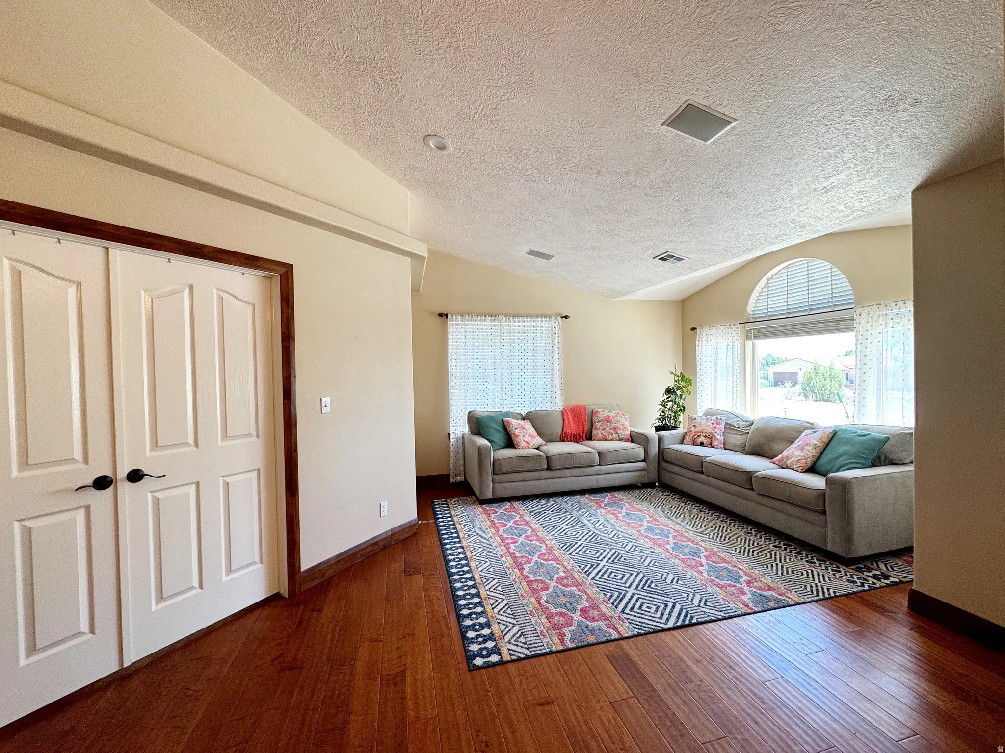 Vaulted ceiling with an arched window, wood-finish flooring, and recessed lighting