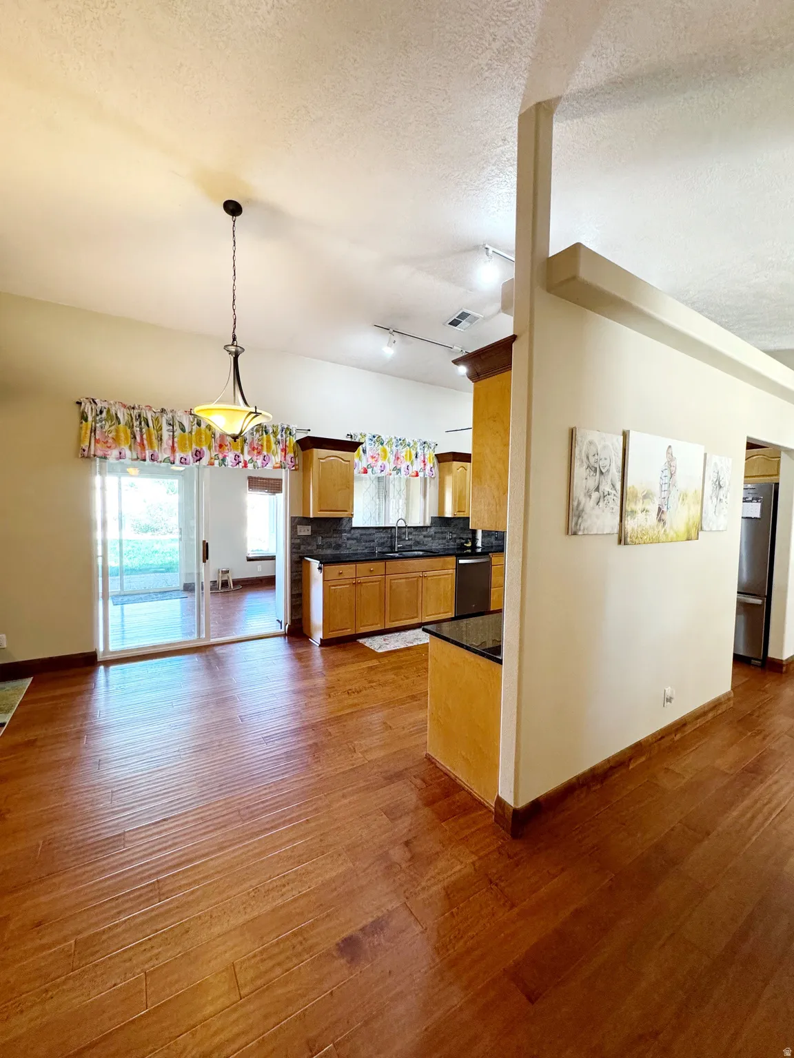 Wood-finish flooring, kitchen cabinetry, dark countertops, built-in appliances, and sliding glass doors