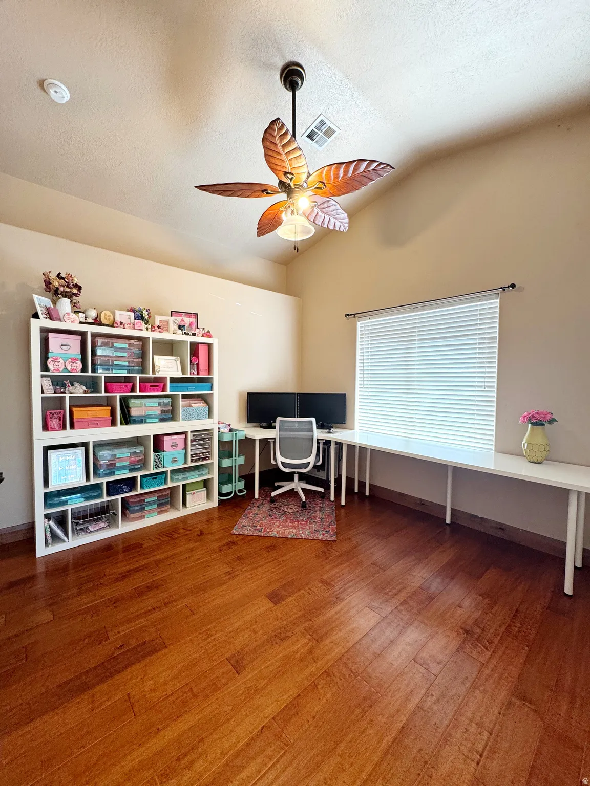 Vaulted ceiling with a decorative ceiling fan, wood-finish flooring, and a built-in L-shaped desk